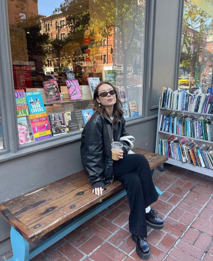 a woman sitting on a bench in front of a book store holding a cup of coffee