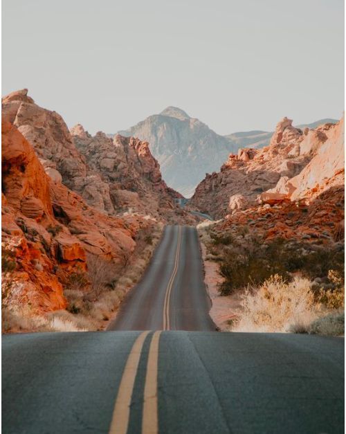 an empty road in the desert with mountains in the backgrounnd and no cars on it