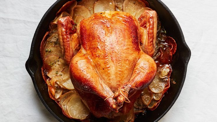 a roasted turkey in a cast iron skillet with potatoes and onions on the side