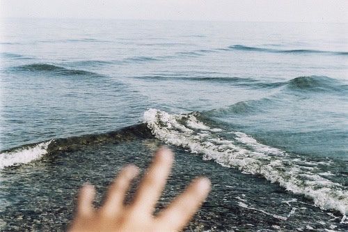 a person's hand reaching out towards the ocean