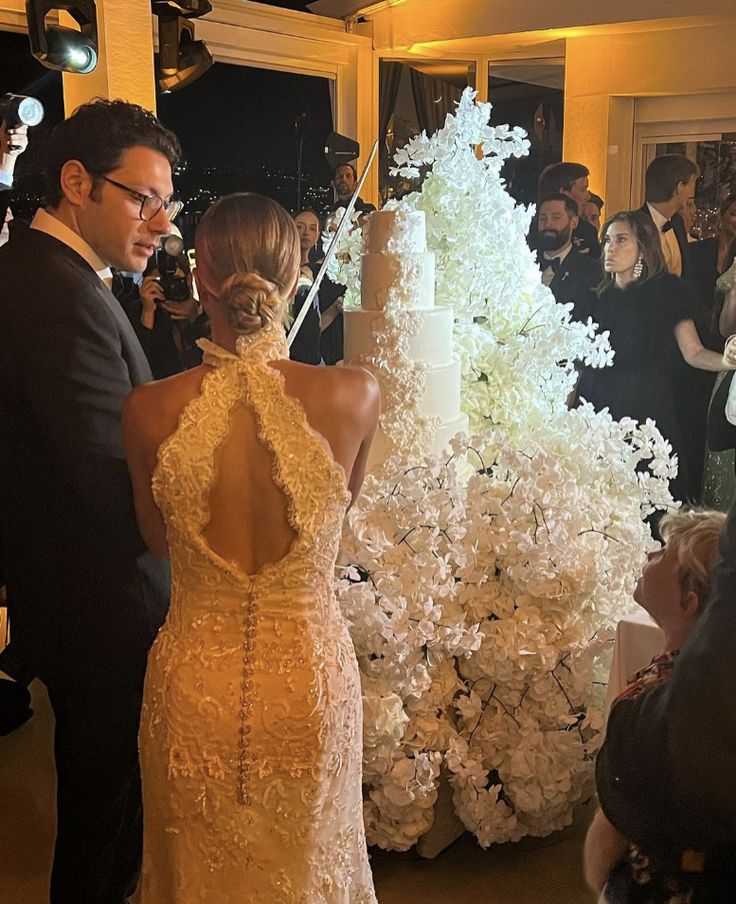 a man and woman standing in front of a tall white cake with flowers on it