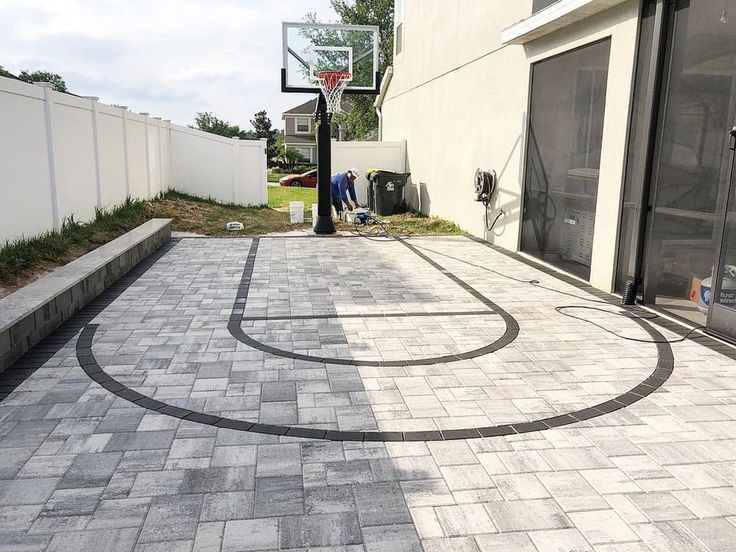 an outdoor basketball court in the middle of a backyard with a man standing on it