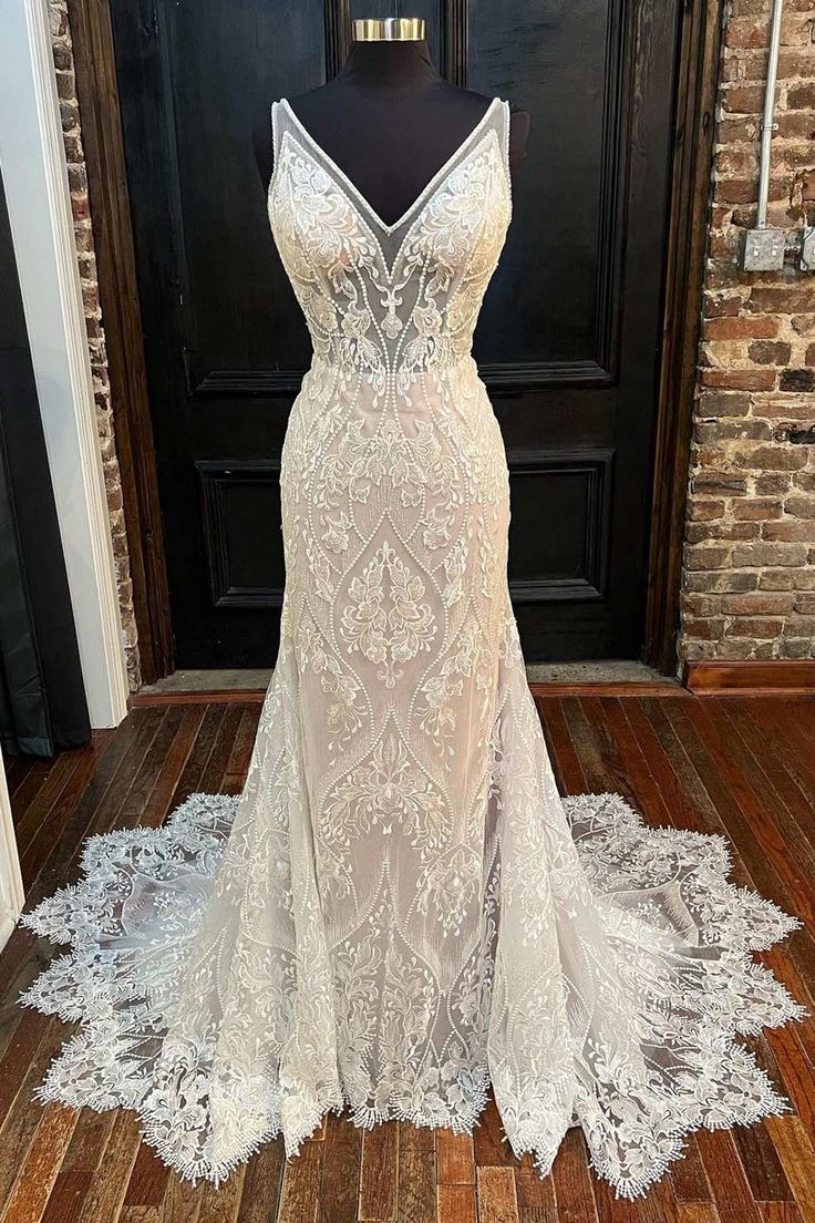 a white wedding dress on display in front of a black door and brick wall behind it