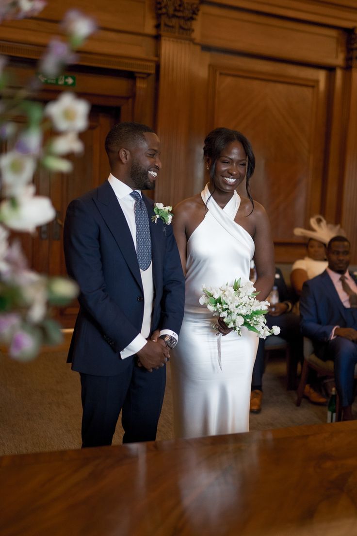 a bride and groom smile as they stand in front of an audience at a wedding ceremony