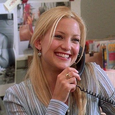 a woman sitting at a desk talking on the phone and smiling while holding a cell phone to her ear