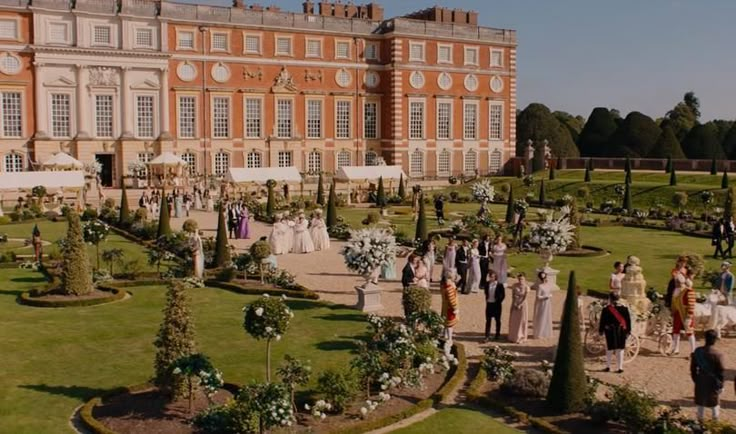 a group of people standing in front of a large building with lots of trees and bushes