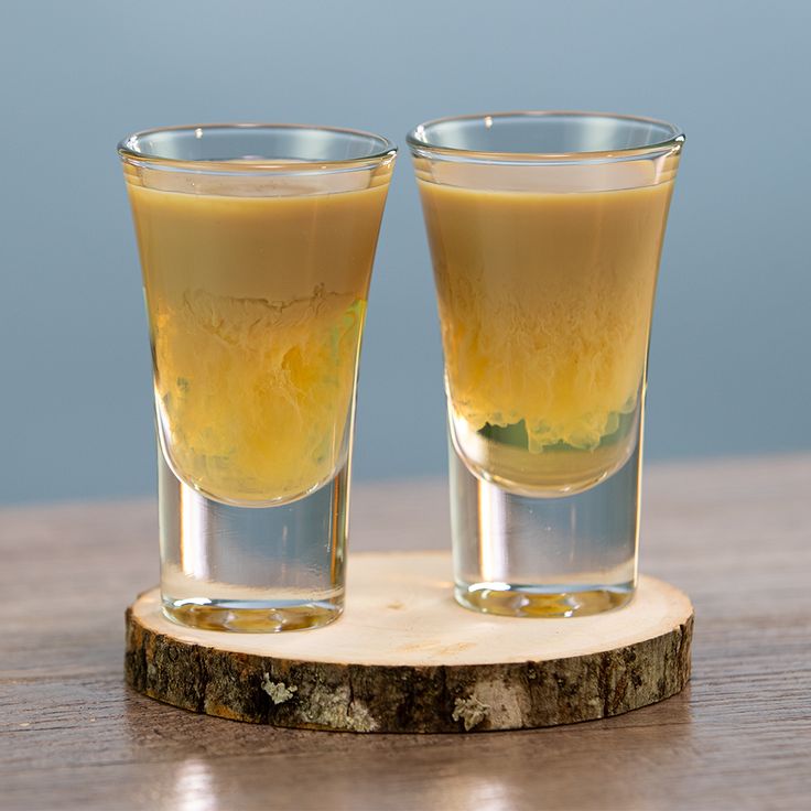 two shot glasses sitting on top of a wooden table next to each other with liquid in them