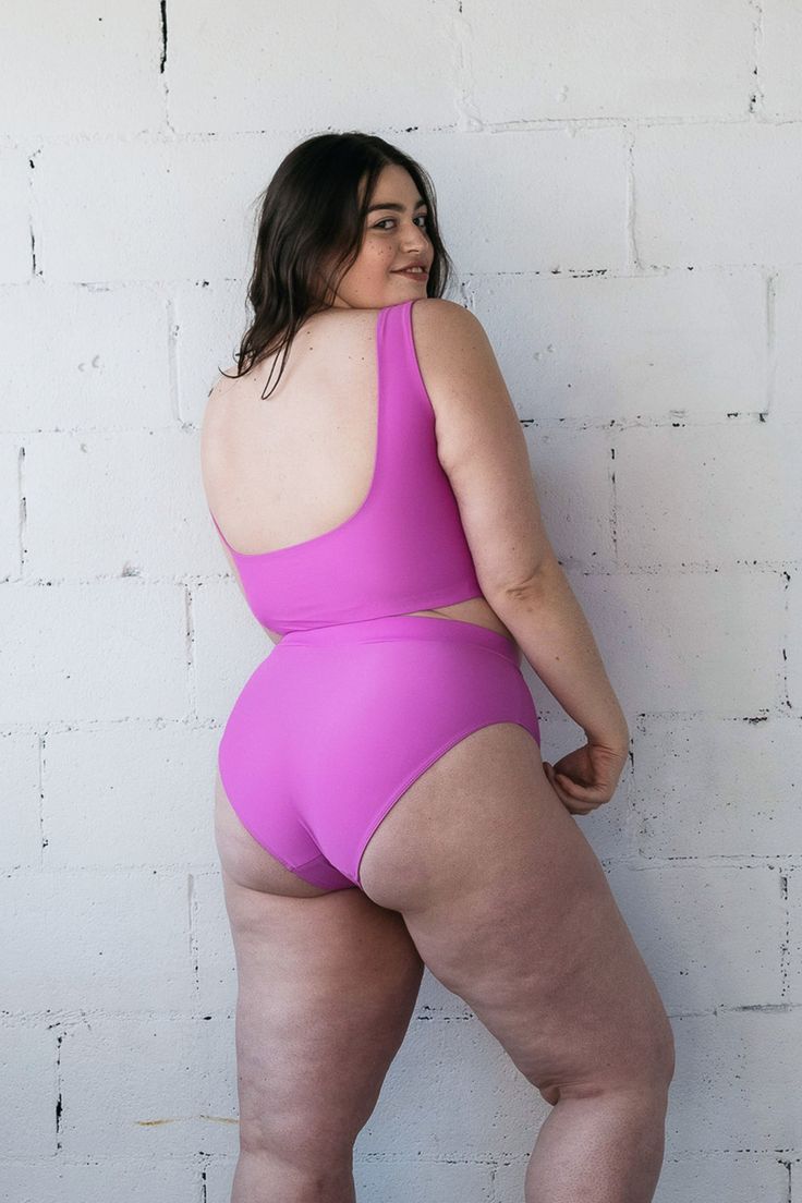 A woman standing in front of a white wall wearing a bright purple swimsuit featuring thick bikini straps for support and high waisted full coverage bottoms. Pink Second-skin Swimwear With Lined Body, Bra Friendly Sleeveless Shapewear Swimwear, Sleeveless Solid Swimwear With Built-in Padding, Solid Sleeveless Swimwear With Built-in Padding, Solid Color Sports Swimwear With Wide Straps, Full Coverage Second-skin Swimwear, Bra Friendly, High Stretch Scoop Neck Swimwear With Built-in Bra, Compressive Sleeveless Swimwear, Bra Friendly, Compressive Sleeveless Swimwear With Bra-friendly Design