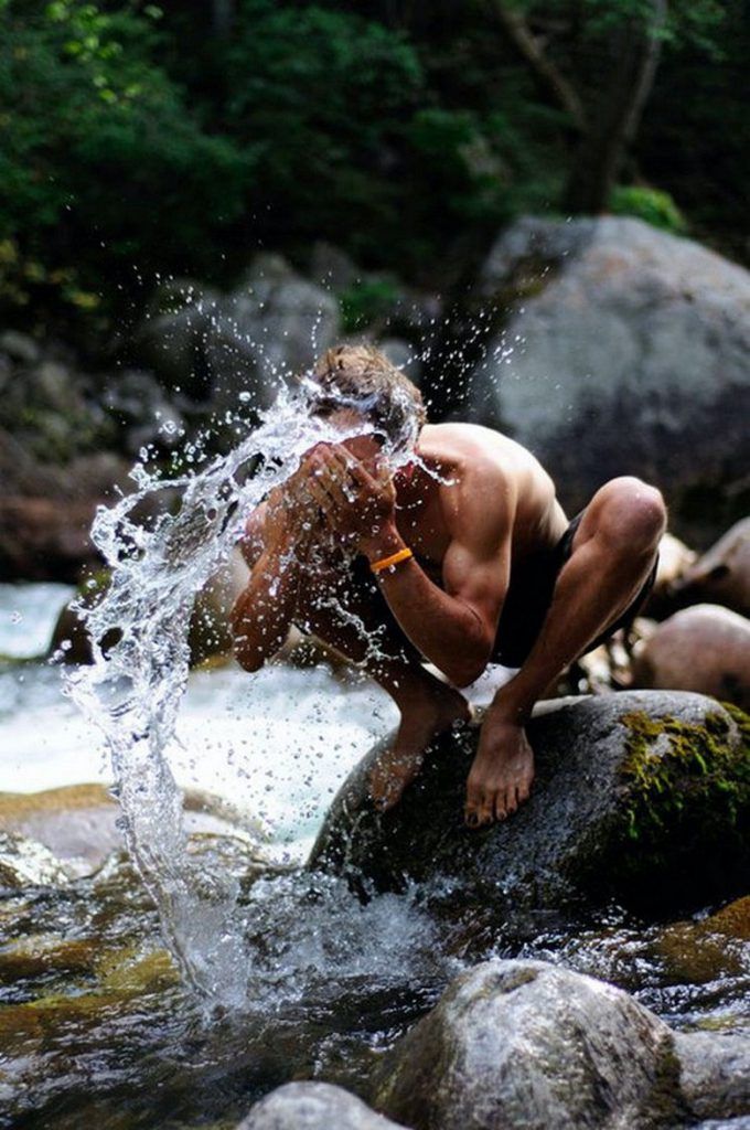 a shirtless man splashing water on rocks in the river