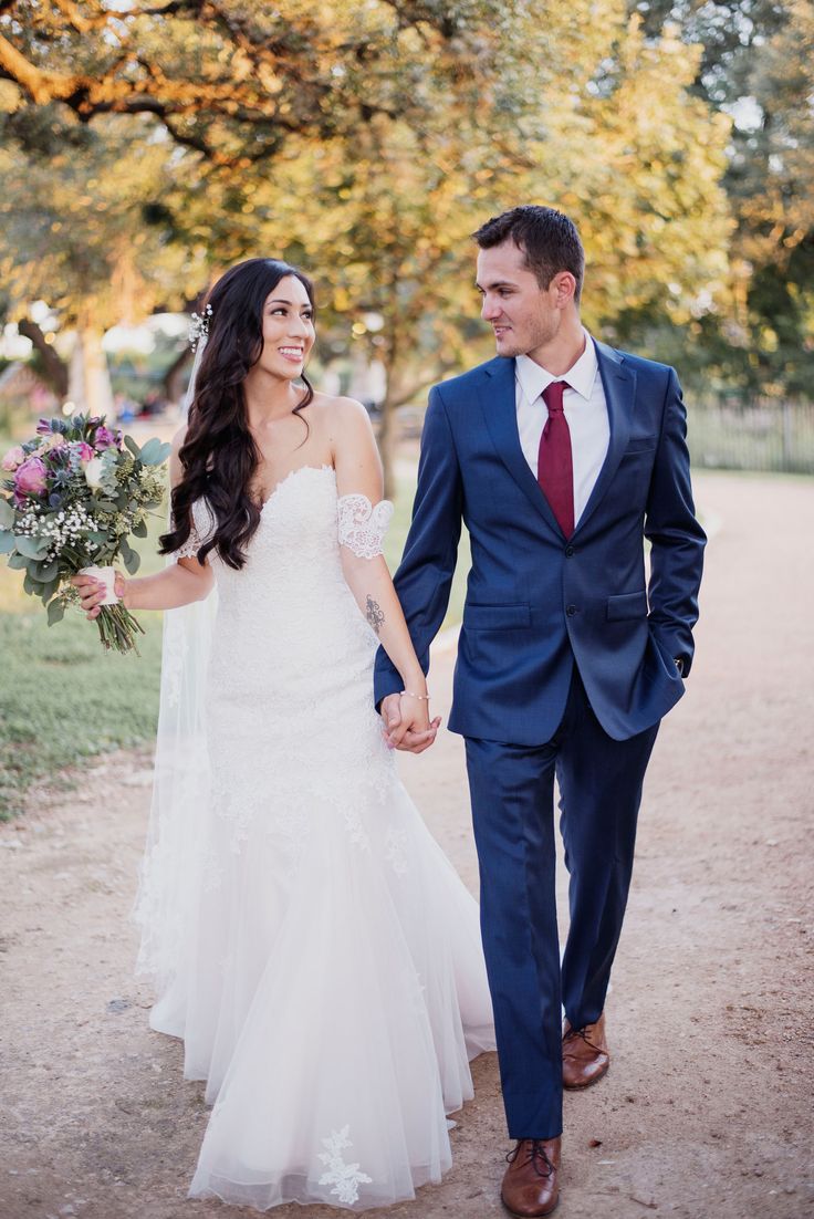 a bride and groom holding hands walking down a path