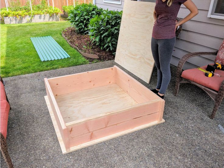 a woman standing next to a wooden box on top of a cement floor in front of a house