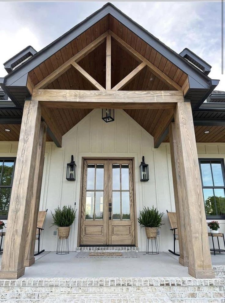 the front entrance to a home with two chairs and potted plants