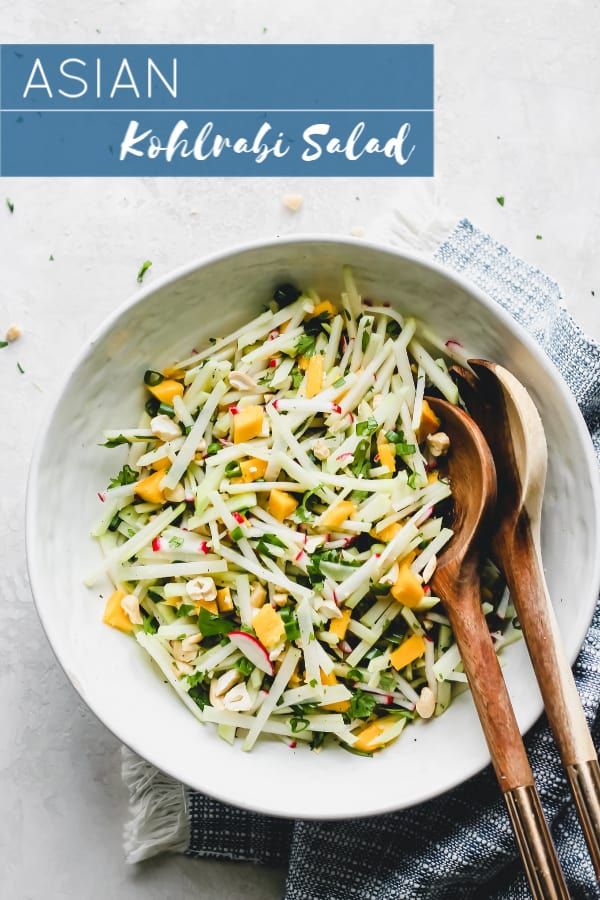 a white bowl filled with coleslaw salad next to two wooden spoons on top of a blue and white towel