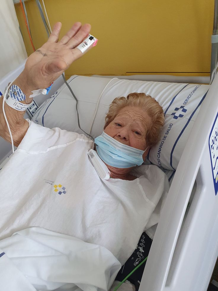 an older woman laying in a hospital bed wearing a face mask