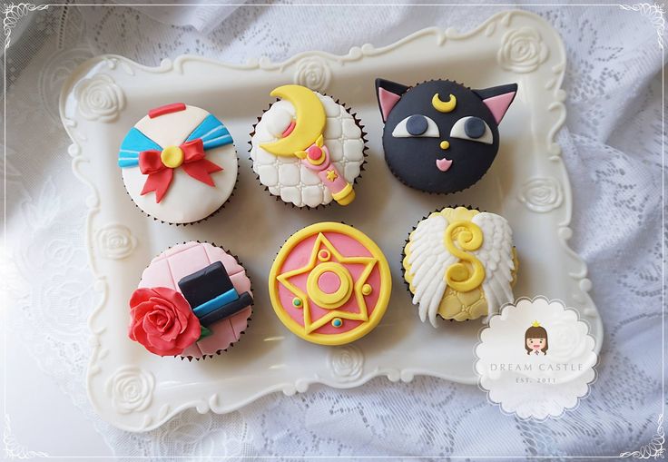 nine decorated cupcakes on a white tray with an angel, cat, moon and star decoration