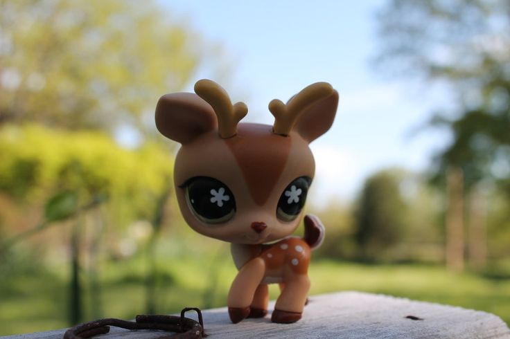 a little deer doll with big eyes on a wooden surface in front of some trees