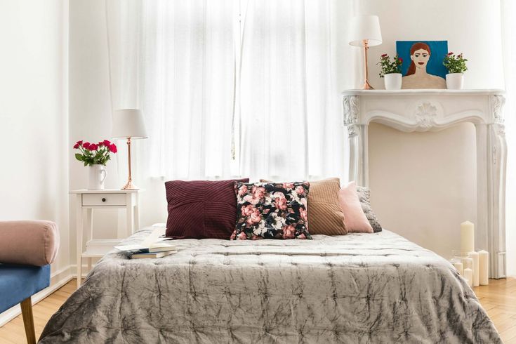 a bed with pillows on it in front of a window next to a blue chair