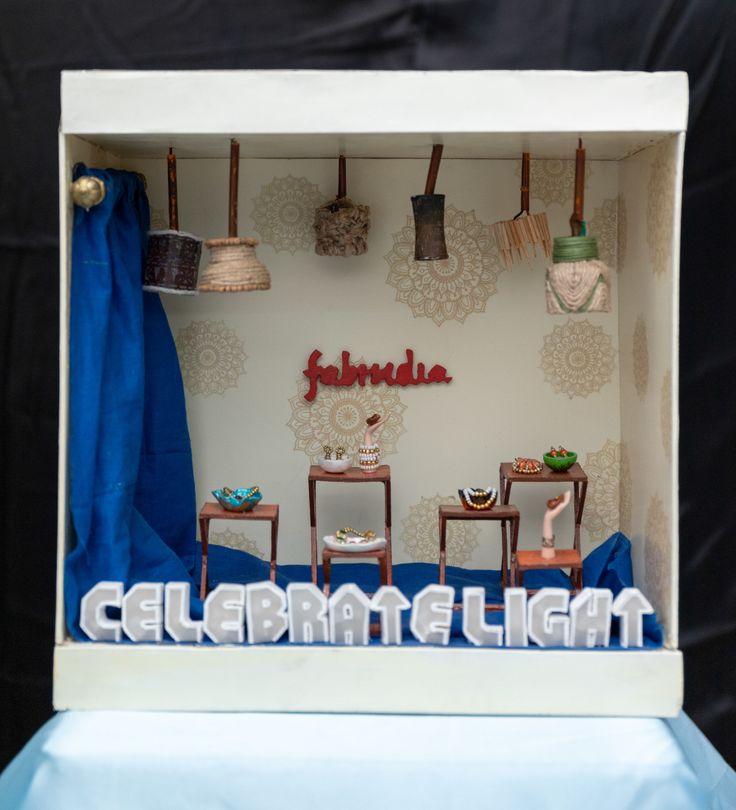 an open box with some decorations on the top and blue curtains behind it, in front of a black backdrop