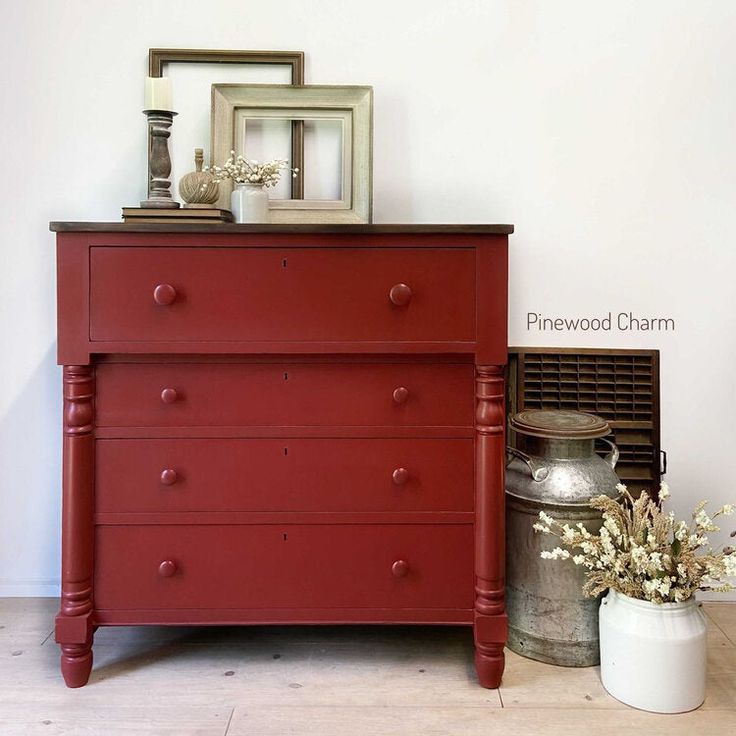 a red dresser sitting next to a white vase with flowers in it and a framed picture on top