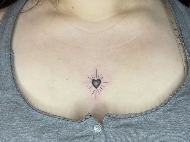 a woman's chest with a small heart tattoo on the left side of her chest