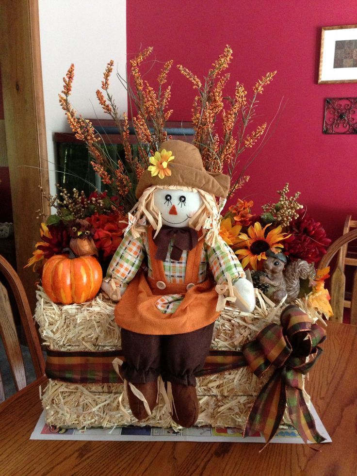 a scarecrow sitting on hay with pumpkins and flowers