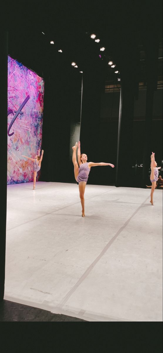 three dancers performing on stage in front of a large painting