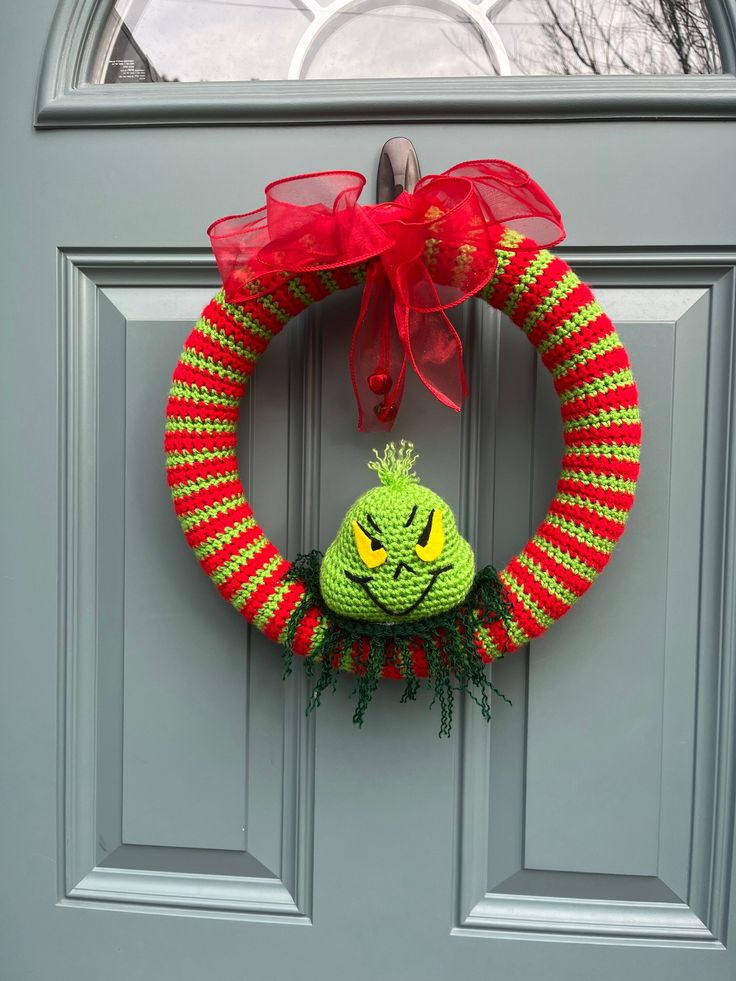 a green and red knitted christmas wreath hanging on a front door with a grin face