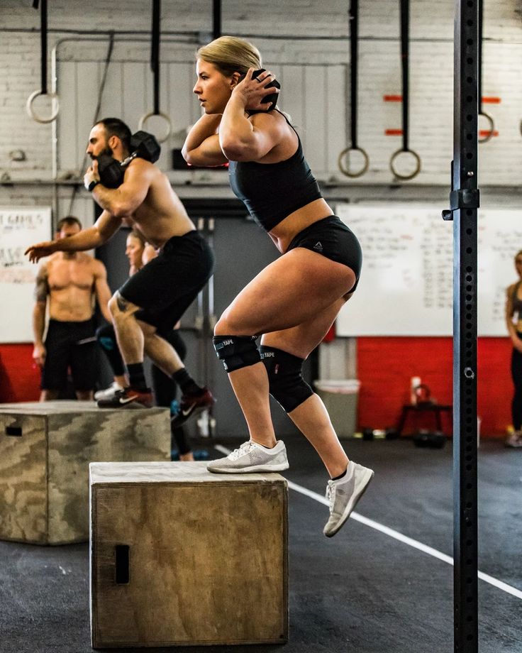 a woman is doing squats on a box in a gym while other people watch