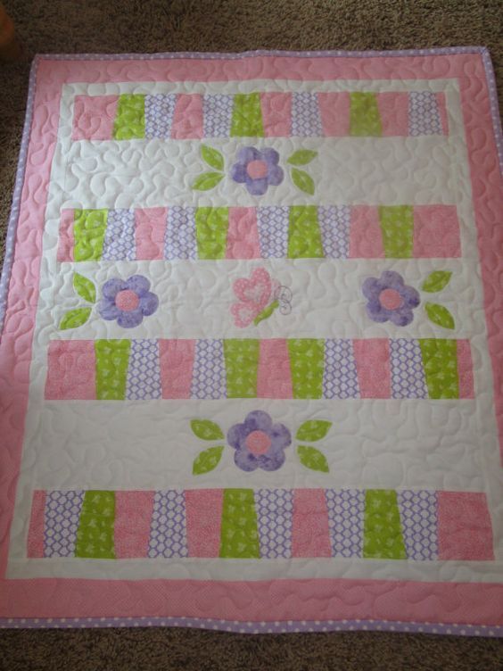 a pink and green quilt with flowers on the border is laying on the floor next to a teddy bear