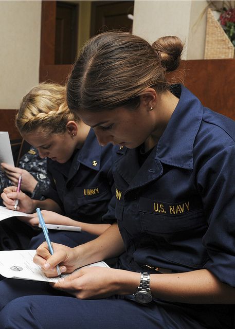 two women in navy uniforms sitting down writing on notebooks and taking notes from each other