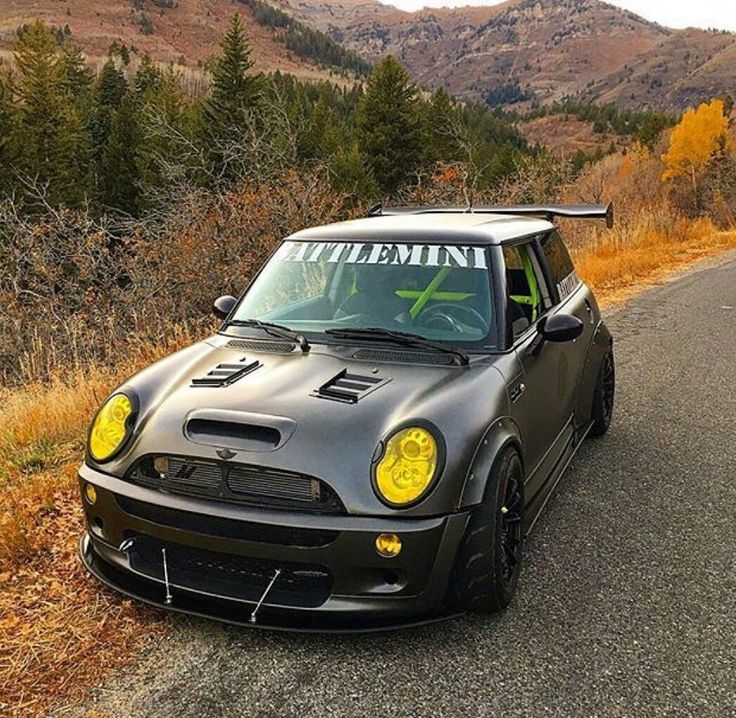 a small black car is parked on the side of the road with mountains in the background