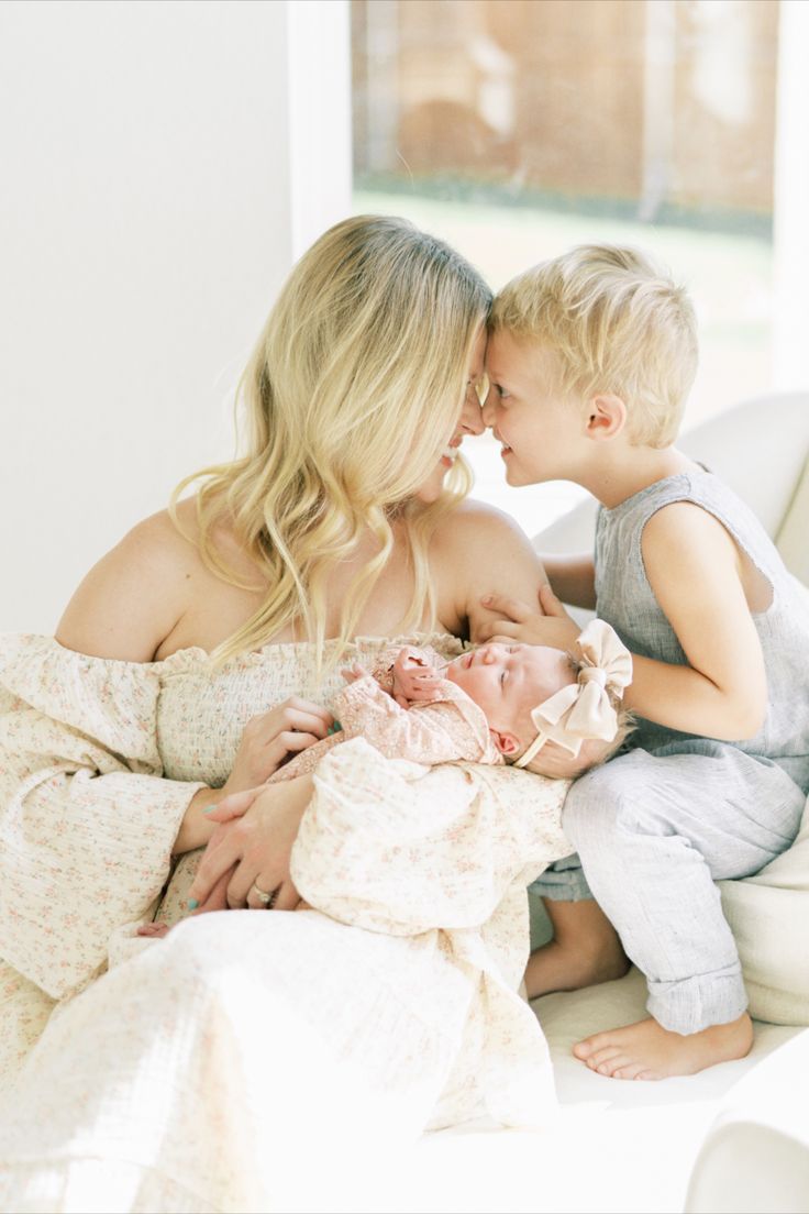 a mother kissing her son's forehead while he is holding his sleeping newborn baby