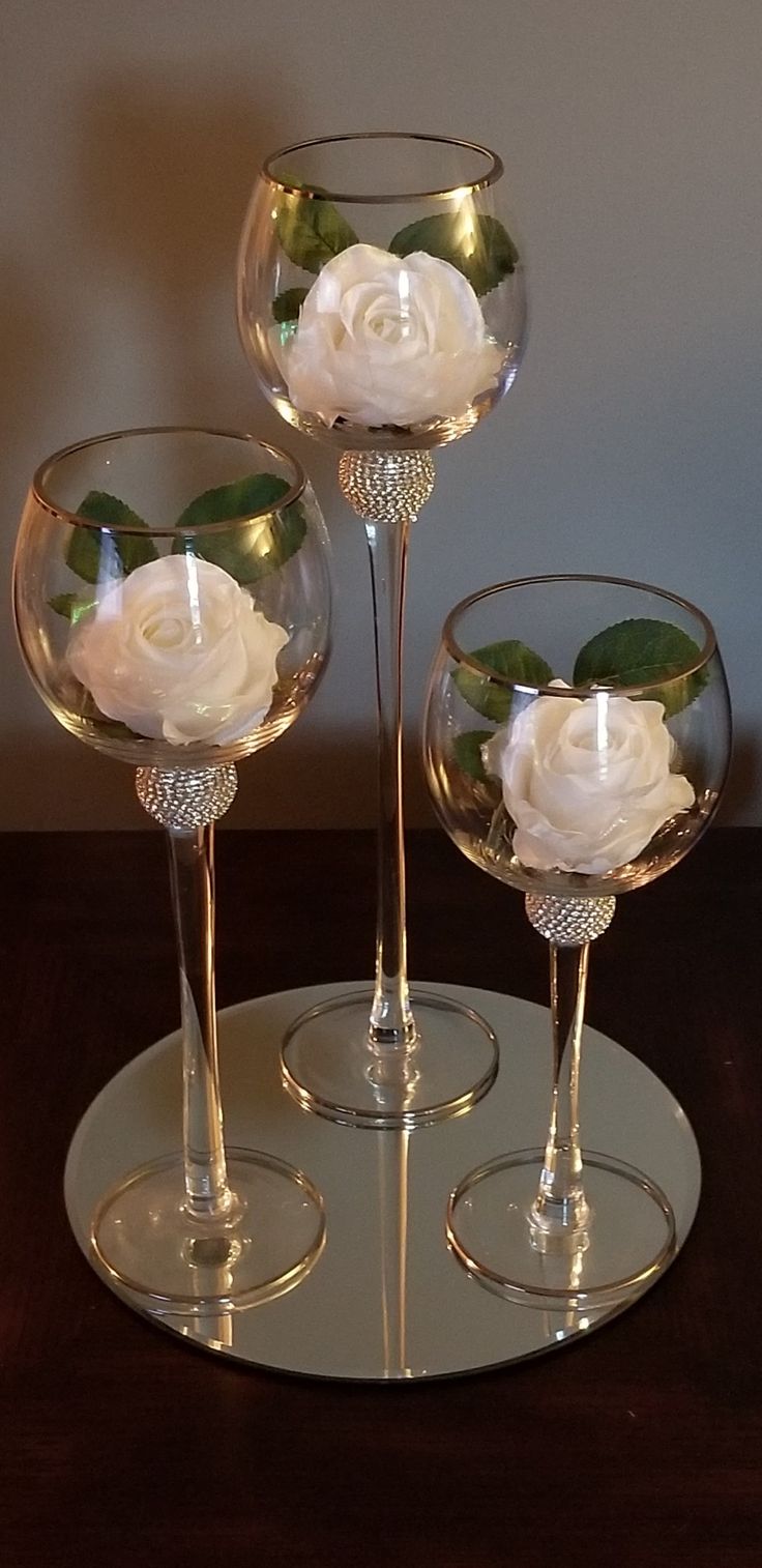 three wine glasses with flowers in them sitting on a table next to a candle holder