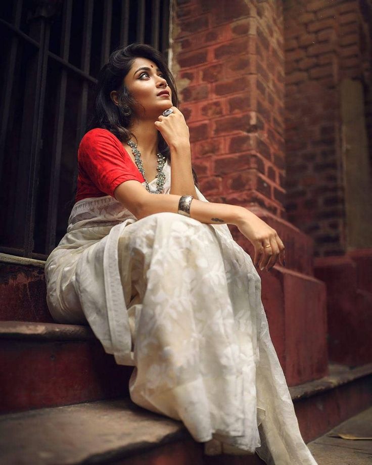 a woman sitting on the steps in front of a brick building with her hand under her chin