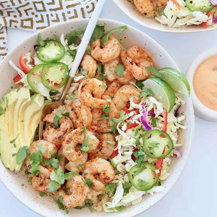 two white bowls filled with shrimp and rice salad next to a bowl of guacamole