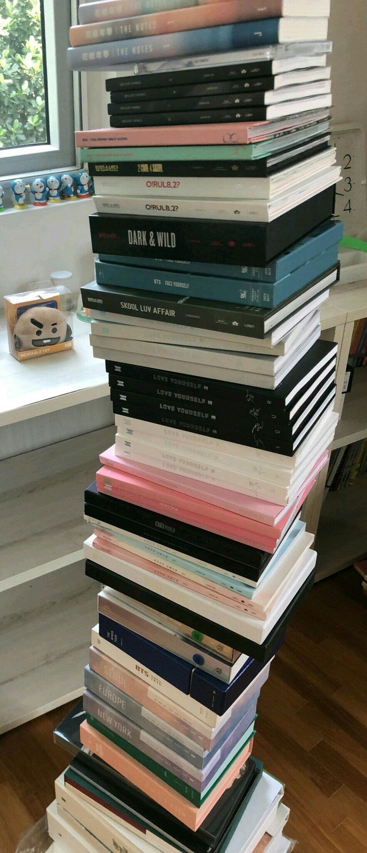 a stack of books sitting on top of a hard wood floor next to a window