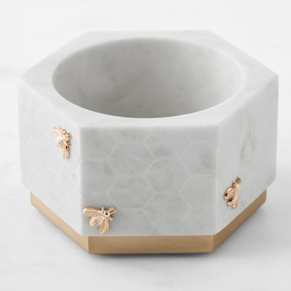 a white marble bowl with gold bee decorations on the rim and bottom, in front of a white background