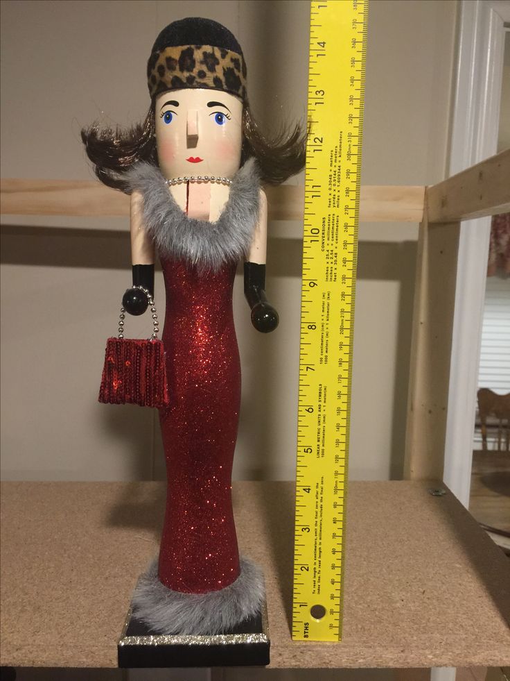 a wooden doll with a red dress and fur stoler next to a measuring ruler