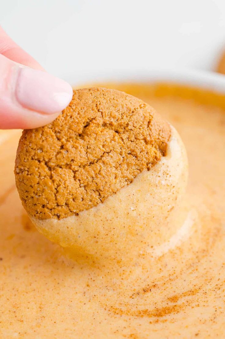 a hand dipping a cookie into a bowl of pumpkin soup with a bite taken out