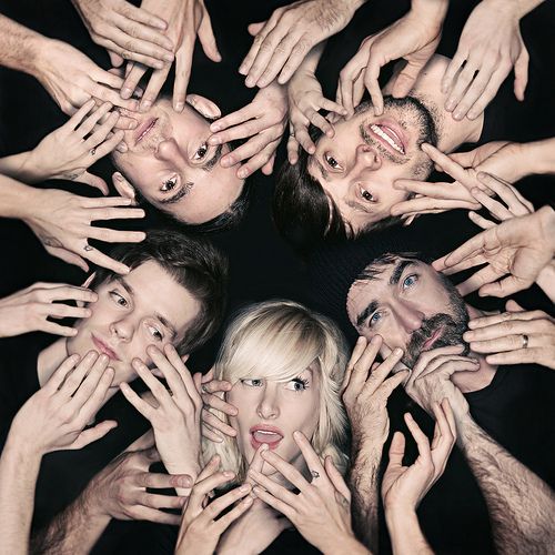 a group of people holding their hands up in the air with one woman's face surrounded by her hands