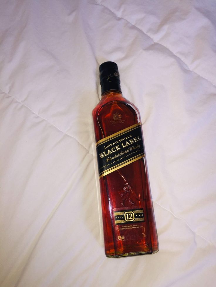 a bottle of whisky sitting on top of a white bed cover covered in sheets and pillows