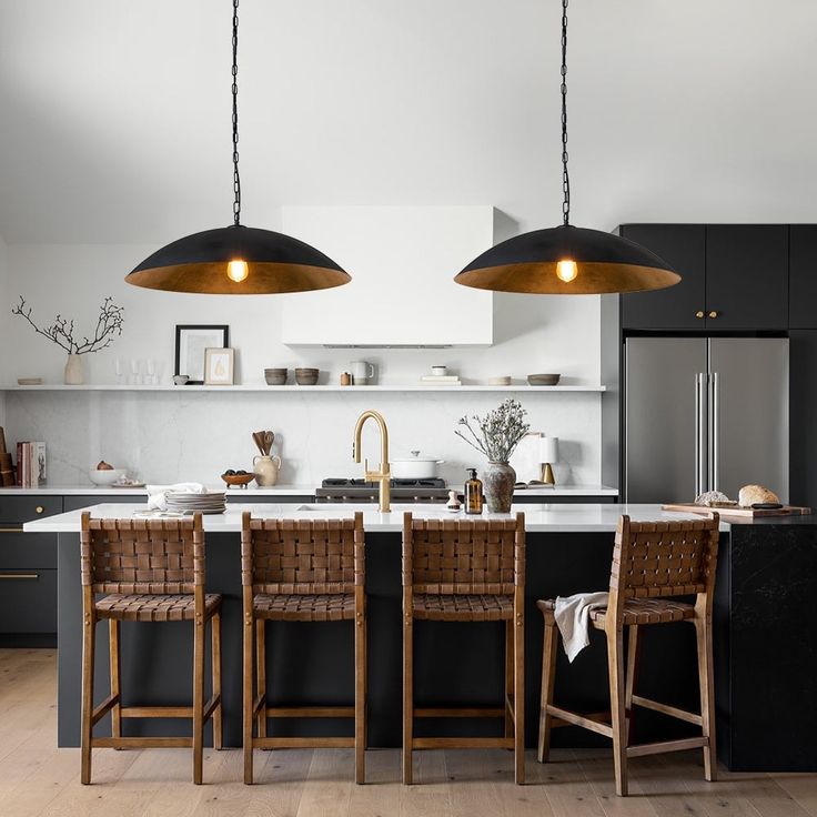 two pendant lights hanging over a kitchen island with chairs and counter tops in front of it