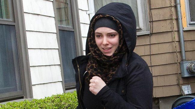 a woman wearing a black jacket and scarf standing in front of a house with a blue motorcycle