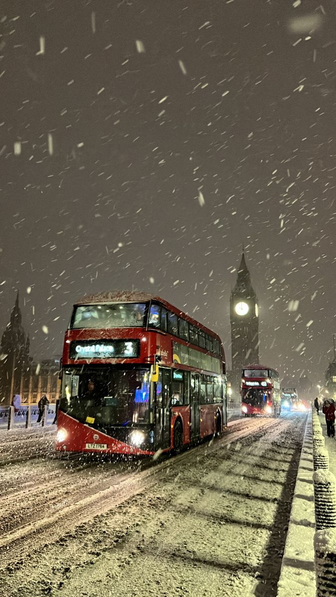 a double decker bus driving down a snow covered street next to a tall clock tower