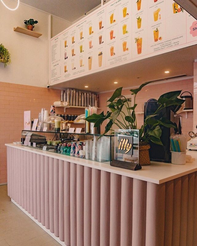 a pink counter in a restaurant with plants on the top and menus above it