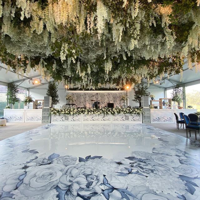 an indoor wedding venue decorated with flowers and greenery hanging from the ceiling, surrounded by blue chairs