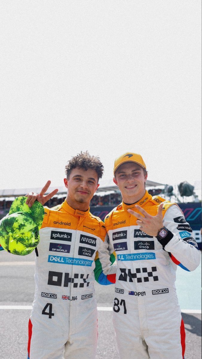 two men standing next to each other in front of a race track with their hands up