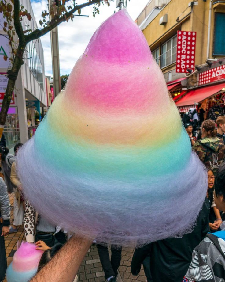 a man is holding up a rainbow colored cotton candy cone in the middle of a crowded street