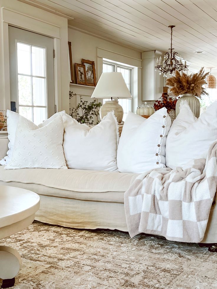 a living room filled with lots of white furniture and pillows on top of a rug