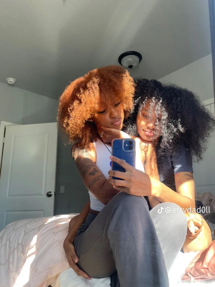 two women sitting on top of a bed looking at a cell phone